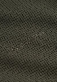 Olivovo zelená textúrovaná látka s pásikavým vzorom, ktorá má reliéfne logo blízko spodnej časti. Materiál pôsobí ľahko a priedušne.