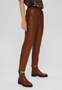 Bruine nep leren broeken met een koord taille, zijzakken en taps toelopende benen, gecombineerd met bruine enkelaarsen met een zijrits.