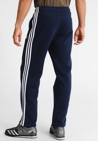 Marineblaue Jogginghose aus weichem Stoff mit drei weißen Streifen an den Seiten. Elastischer Bund mit normaler Passform.