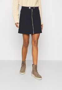 Černá minisukně s předním zipem, texturovaná tkanina a boční kapsy. Vybaveno taupe kotníkovými botami s klínovou podrážkou.