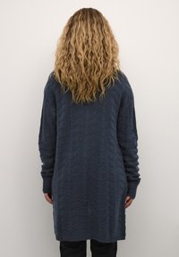 Marineblå strikket cardigan med en chevron-mønster, lange ermer og ribbestrikkede mansjetter, med en rett skjæring som strekker seg under hoftene.