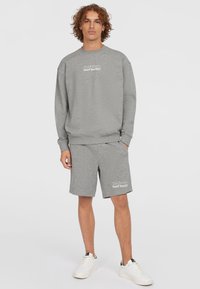 Grijze sweatshirt en shorts van zacht materiaal. De sweatshirt heeft een ronde hals en witte tekst, de shorts hebben een elastische tailleband en zijzakken.