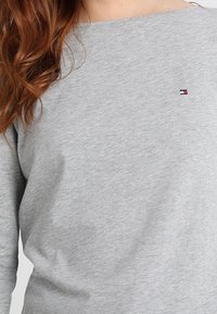 Grå sweatshirt med båtringning, tillverkad av bomull. Har en liten broderad logotyp i röd, vit och blå färg på bröstet.