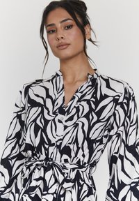Vestito a fantasia bianco e nero con colletto, maniche lunghe, dettagli con bottoni e una cintura a cravatta, realizzato in un tessuto leggero e fluido.