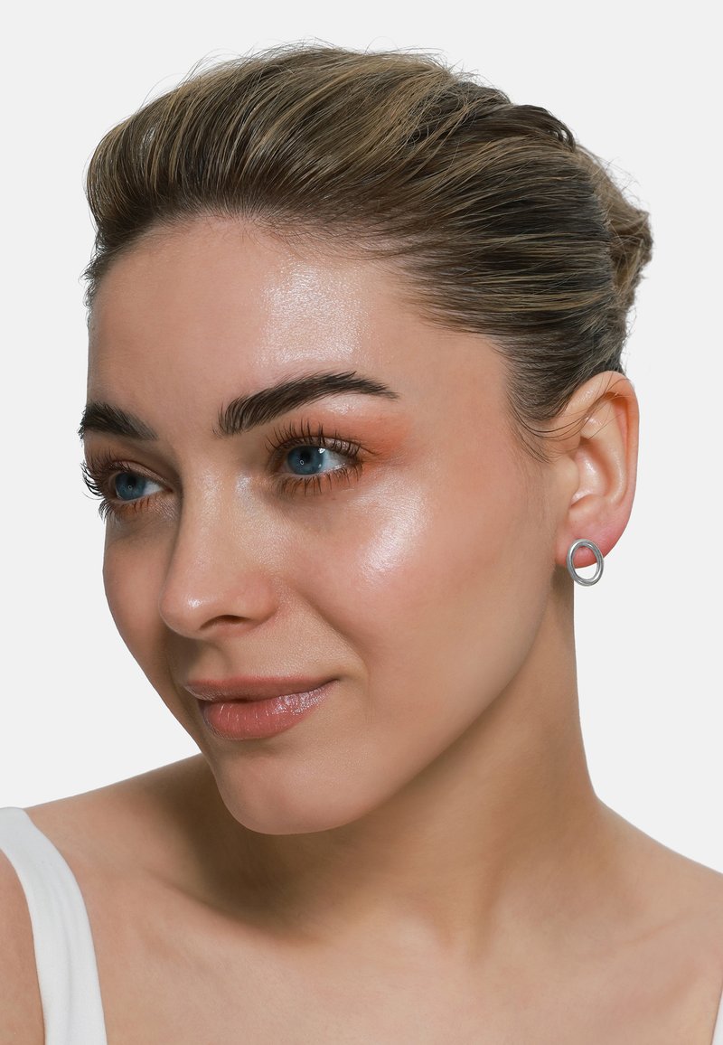 Silberne Creolen mit einem kreisförmigen Design, glatter Textur und polierter Oberfläche, präsentiert von einem Model vor einem schlichten Hintergrund.