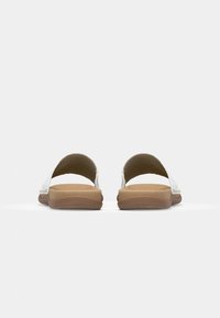 Bílé skluzné sandály s minimalistickým designem, měkkou polstrovanou stélkou a svetle hnědou gumovou podrážkou. Obsahují dva široké popruhy pro oporu.