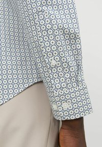 Camicetta con bottoni caratterizzata da un motivo geometrico blu e bianco, maniche lunghe con due bottoni ai polsini e orlo curvato.