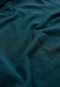 Tissu tricoté teal avec une texture lisse, présentant des plis doux et des variations de couleur subtiles, conçu pour les vêtements.