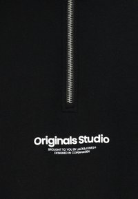 Czarna bluza na zamek z srebrnym zamkiem błyskawicznym i białym napisem: „Originals Studio” oraz napisem poniżej „Prezentowane przez JACK & JONES”.