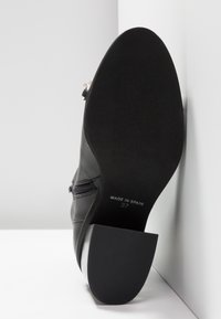 Bottine en cuir noir, présentant un design élégant, un bout pointu, une fermeture éclair latérale et une semelle en caoutchouc texturée. "Made in Spain" et taille 37 imprimés.