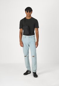 Camiseta negra de manga corta, jeans desgastados de un azul claro y zapatillas negras con acentos blancos. Se lleva un pequeño bolso negro cruzado.