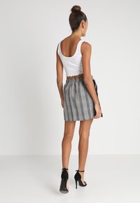 Un top court blanc associé à une jupe à carreaux grise avec une taille élastique et un détail de lien sur le côté. Le modèle porte des escarpins noirs.