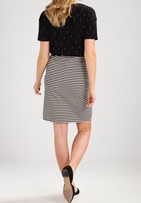 Haut noir à manches courtes avec des motifs verticaux, associé à une jupe noire et blanche à rayures de longueur genou. Modèle portant des escarpins noirs.