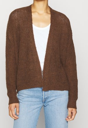 Cardigan marron à manches longues en tissu tricoté texturé, avec un devant ouvert et une coupe décontractée, porté sur un haut blanc et un jean.