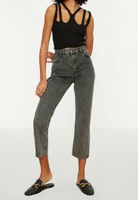 Top corto negro acanalado con tirantes cortados, jeans de mezclilla gris de tiro alto y zapatos negros de tela trenzada con acentos dorados.