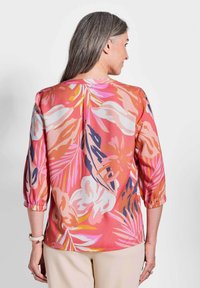 Blumenbluse in Rosa, Orange und Weiß. Verfügt über Dreiviertelärmel, geraffte Bündchen und einen glatten, leichten Stoff mit einem tropischen Muster.