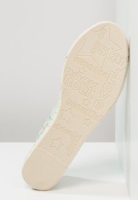 Suola delle scarpe in beige con superficie testurizzata, caratterizzata da parole in rilievo come "ROCK," "LOVE," e "VISION," insieme a motivi stellari.