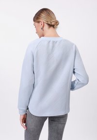 Felpa azzurra chiara con un motivo a zigzag testurizzato, polsini a coste e orlo arrotondato. Abbinata a pantaloni grigi aderenti.