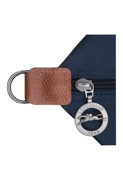 Navy blue nylon zippered bag corner with textured brown leather accent, silver hardware, and circular silver charm marked 'LONGCHAMP 1948'.