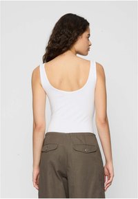 Top bianco senza maniche con scollatura sul retro, abbinato a pantaloni larghi verde oliva con due tasche posteriori e chiusura a bottone.