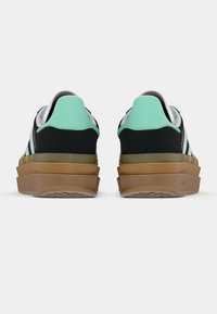 Par de zapatillas negras con lengüetas traseras de color verde menta, rayas blancas en los costados y suelas de goma marrón estratificadas vistas desde atrás.