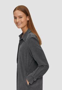 Graue Langarmshirtjacke mit spitzem Kragen, seitlichen Taschen und einem weichen, strukturierten Stoff. Gerader Schnitt, lässiges Design.