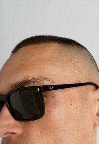 Ochelari de soare dreptunghiulari negri, cu lentile întunecate, logo-ul Ray-Ban pe ramă, având un design elegant și o finisare lucioasă.