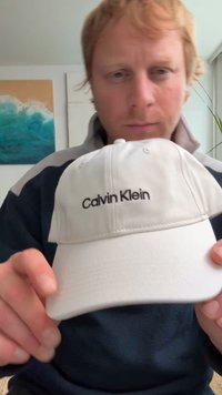 Λευκό καπέλο μπέιζμπολ με μαύρο λογότυπο "Calvin Klein" μπροστά. Το ύφασμα είναι λείο, με κυρτό γείσο και ρυθμιστή πίσω.