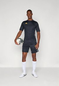 Tummanharmaa urheilupaita ja shortsit kultaisella logolla, valkoiset sukat ja jalkapallo. Urheilullinen istuvuus ja sileä materiaali.