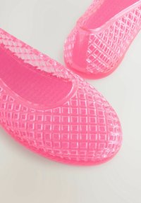 Flats en gelée translucides rose vif avec un motif quadrillé texturé sur fond blanc.