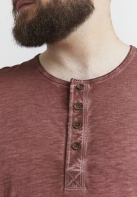 Maglietta henley amaranto in tessuto morbido, con scollatura rotonda, cinque bottoni marroni sul davanti e una finitura texturizzata.