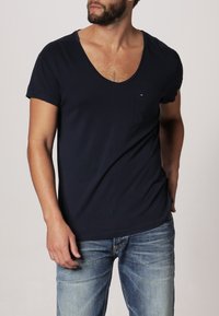 Granatowa bawełniana koszulka z głębokim dekoltem w kształcie litery V i krótkimi rękawami, z małą kieszonką na piersi i akcentem z logo na kieszeni.