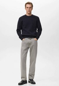 Mornarica pulover in svetlo sivi kavbojke. Pulover ima okroglo izreznico in rebraste manšete; kavbojke so ravne kroja z gladko teksturo. Črne čevlje.