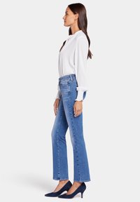 Blusa blanca ligera de manga larga combinada con jeans de mezclilla azul de tiro alto y zapatos de tacón alto de ante azul marino.