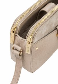 Beżowa torebka skórzana o teksturowanej powierzchni z podwójnymi złotymi zamkami, dopasowanym paskiem ze złotymi kółkami oraz delikatnym grawerem marki na uchwytach zamków.