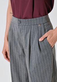 Grau gestreifte Hose mit hoher Taille, Falten und Knopfdetail. Hergestellt aus leichtem Stoff, mit seitlichen Taschen.