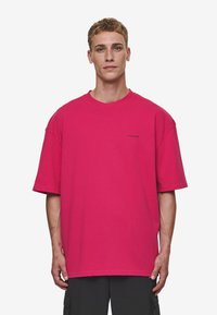 Pink oversized T-shirt made of cotton, featuring short sleeves, a round neckline, and a small logo detail on the chest.