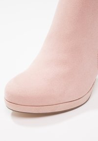 Bottine en daim rose clair avec bout arrondi et légère semelle compensée sur fond blanc.