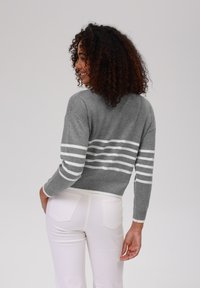 Pulover tricotat gri cu dungi orizontale albe, design ajustat, manșete și tiv cu nervuri. Asortat cu pantaloni albi, prezentând o vedere din spate.