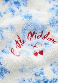 Weicher blau-weißer Batikstoff mit roter, handschriftlicher Stickerei mit dem Text "Mit Kindern" und zwei kleinen roten Kirschen darunter.