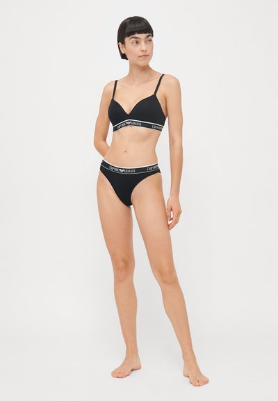 Černý set spodního prádla skládající se z bezešvého podprsenky s nastavitelnými ramínky a výstřihem do V, doplněný o odpovídající vysoké kalhotky, obojí s logem na pasu.