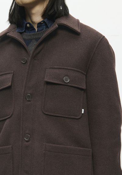 Chaqueta de mezcla de lana marrón con diseño de cuello, dos bolsillos en el pecho con cierres de botón y un acabado texturizado. Detalle de costura visible.