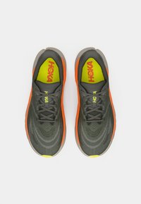 Ein Paar dunkelgraue Laufschuhe mit orangefarbigen Akzenten, gelben Einlegesohlen und "HOKA"-Branding, von oben auf einem weißen Hintergrund betrachtet.