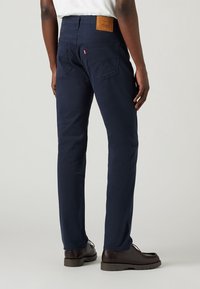Marinblå chinos med rak passform tillverkade av bomull. Har två bakfickor, en beige läderpatch på midjebandet och bruna skor.