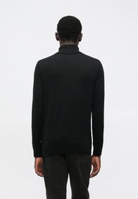 Black sweater with a high collar, long sleeves, and ribbed cuffs. Smooth texture with a relaxed fit, designed for a casual look.