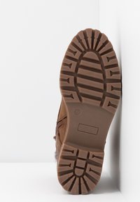 Botte marron avec une semelle extérieure en caoutchouc texturé. Comprend une fermeture éclair latérale et un accent en matière similaire à la laine près de la cheville. Design robuste pour une durabilité optimale.