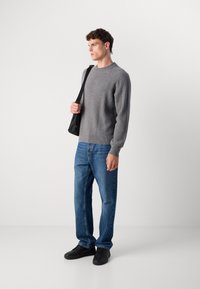 Gray ribbed-knit sweater with a crew neck, paired with blue straight-leg jeans and black sneakers. Model carries a black shoulder bag.