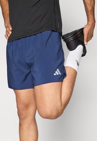 Marineblå treningsshorts med elastisk midjebånd; har en logo med tre hvite striper på nedre venstre side. Brukes med svarte sko og hvite sokker.