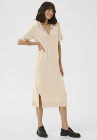 Robe en tricot beige pastel à manches courtes, col polo, fentes latérales et coupe décontractée. Assortie à des chaussures à plateforme noires.