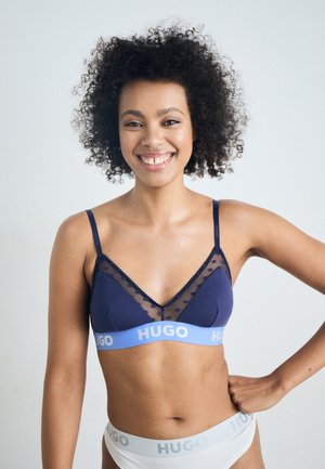 Marineblauwe beha met doorzichtige stippenpanele en verstelbare bandjes. Heeft een zachte elastische band met "HUGO"-branding in lichtblauw.